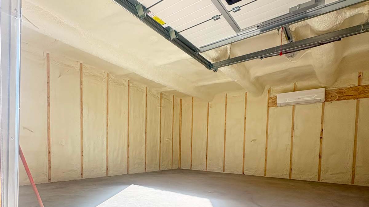 Garaazi soojustamine 4 Unfinished garage with spray foam insulation on walls and vertical studs concrete floor and a mounted mini split unit on the far wall
